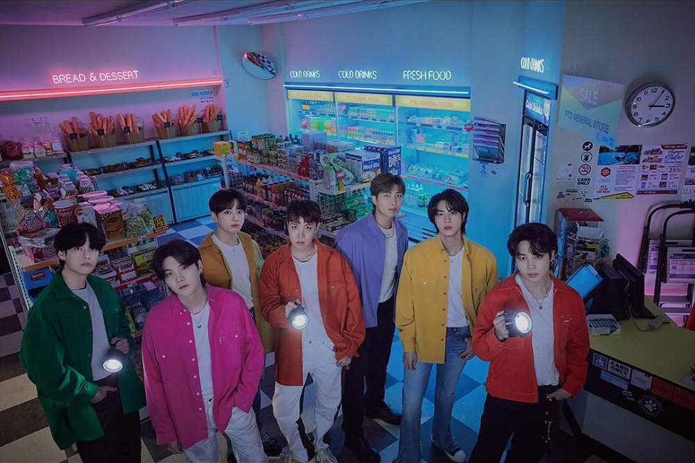 Jin, J-Hope, Jungkook, RM, Jimin, V e SUGA em mercado com roupas e cabelos multicoloridos