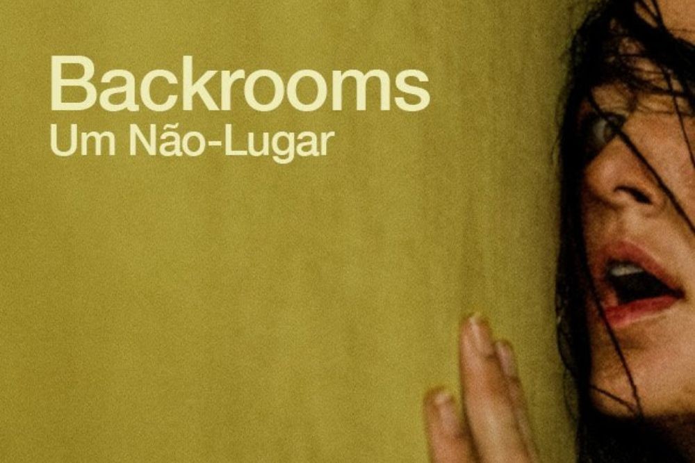 Mulher com expressão de pânico, boca aberta e olhos arregalados, com cabelos escuros e molhados no rosto, encosta a mão na parede amarela. O texto "Backrooms Um Não-Lugar" aparece no canto superior esquerdo