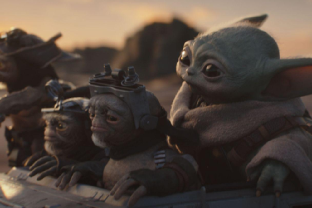 Grogu, o Baby Yoda, em um veículo com três alienígenas pequenos, um deles com barba branca e capacete, olhando para a frente, com um céu alaranjado ao fundo