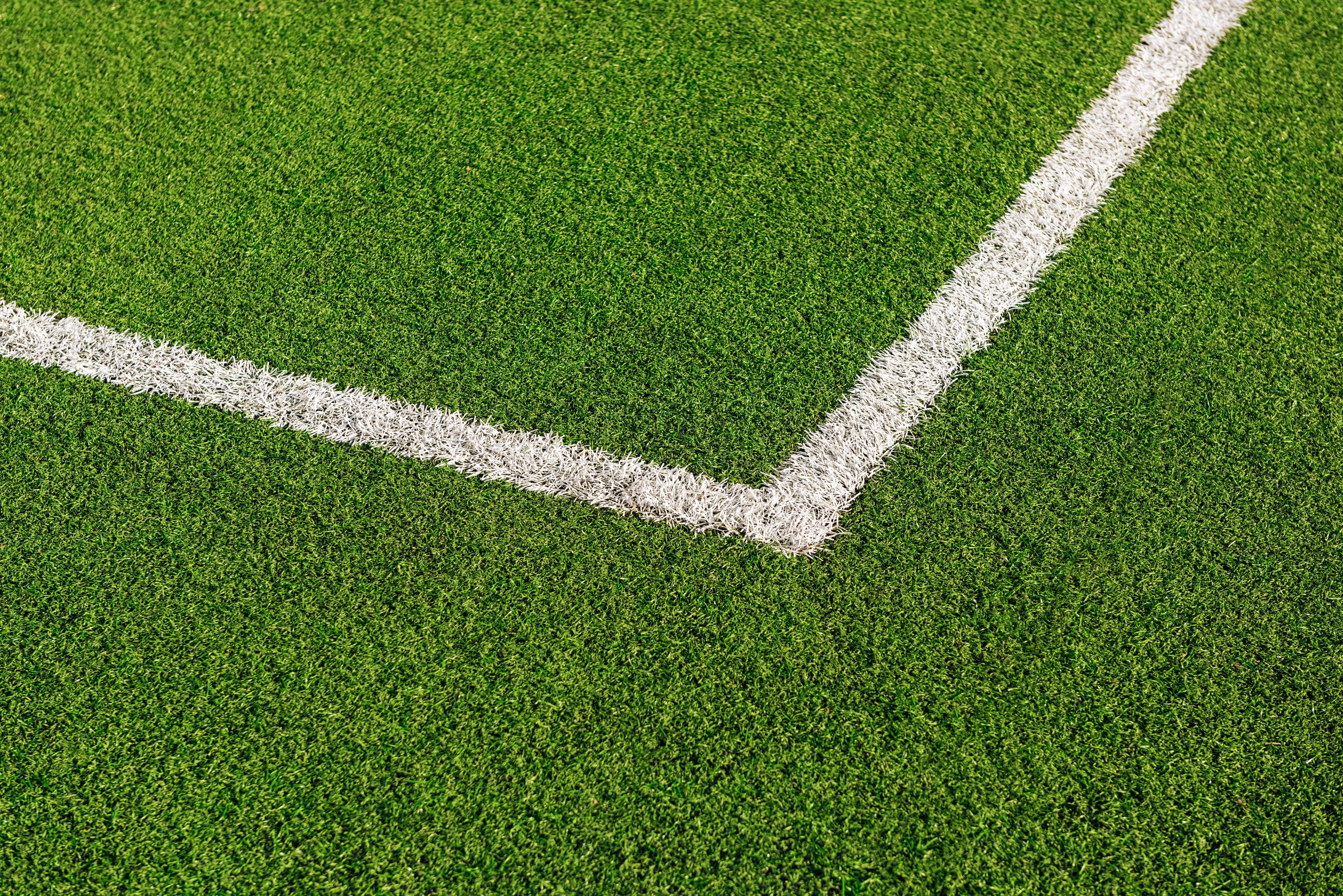 Campo de futebol com gramado sintético verde vibrante e duas linhas brancas marcando um canto do campo