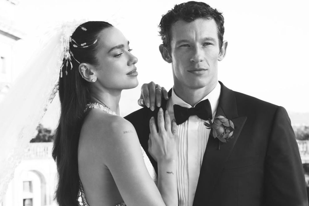 Dua Lipa com véu e vestido de noiva, abraça Callum Turner, que veste terno e gravata borboleta, em foto preto e branco